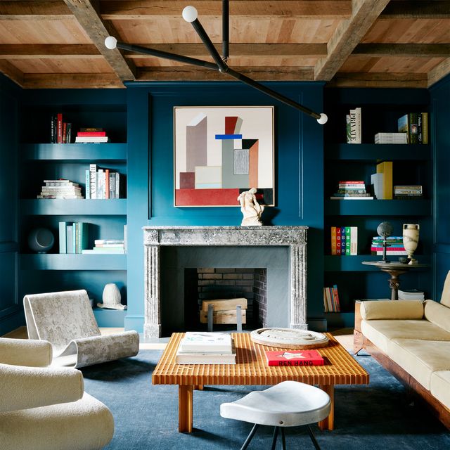 blue painted and carpeted living room with large gray marble mantel at center and modern painting above it built in shelving on either side and accented with low square coffee table and light colored furniture