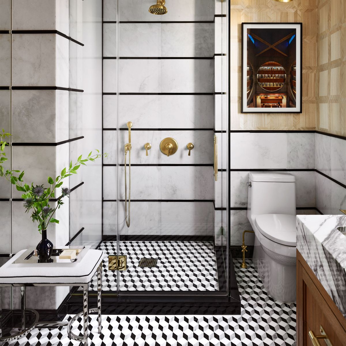 black and white bathroom with three dimensional cube tiles clear shower stall with bronze like fittings in front of the stall is a low stool with chrome legs and a cushion on which rests a tray with a small black vase holding green sprigs