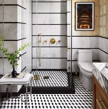 black and white bathroom with three dimensional cube tiles clear shower stall with bronze like fittings in front of the stall is a low stool with chrome legs and a cushion on which rests a tray with a small black vase holding green sprigs