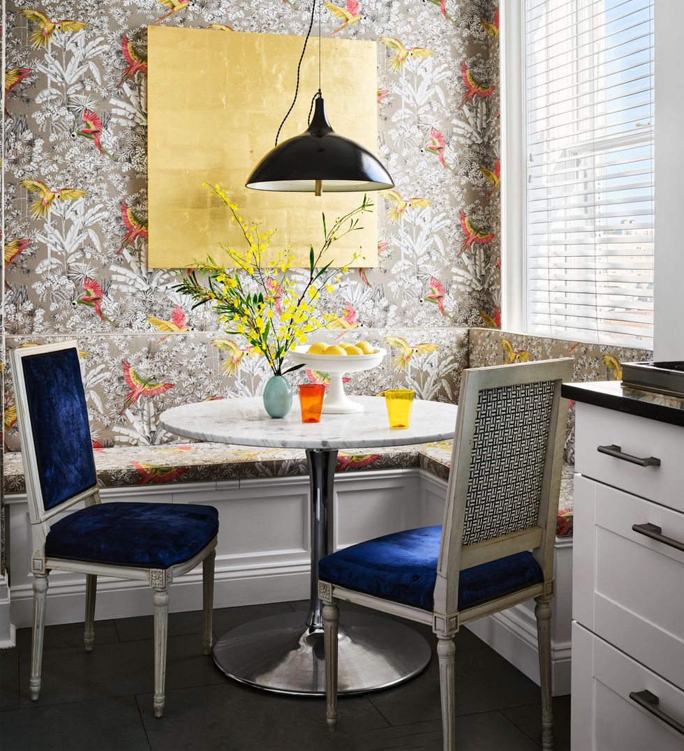 small corner breakfast area covered in a bird themed wallcovering with built in banquette of the same fabric and round white marble table with chrome base and two antique swedish chairs upholstered in dark blue velvet