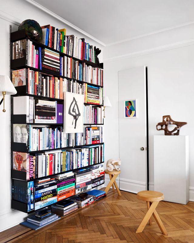 large bookcase against wall filled with books secret door herringbone wood floor and two wooden stools with x shaped legs