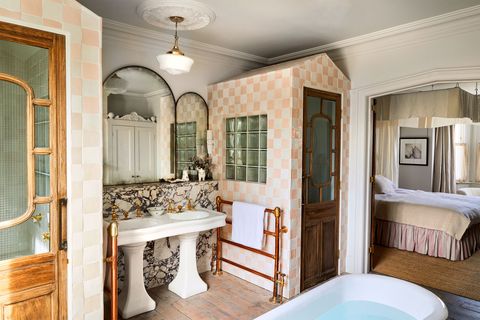 charming bathroom with a shower inset into a small cottage like structure and the sink just outside it and tub in the foreground all connected via an arch to a bedroom in the background