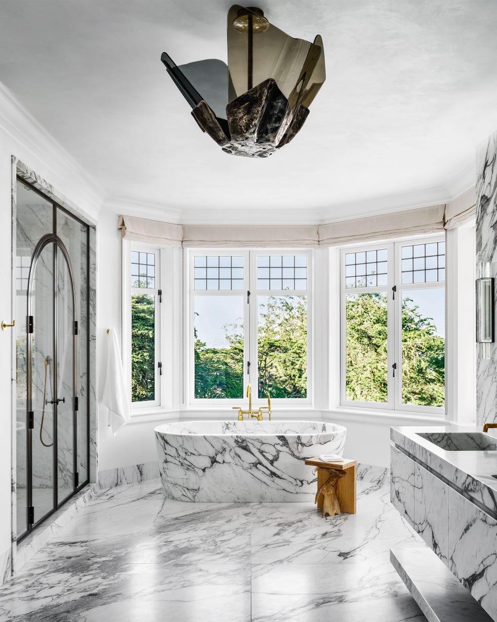 rounded bathroom with double windows in an arc at the back with a standalone marble tub at center and a floating marble vanit