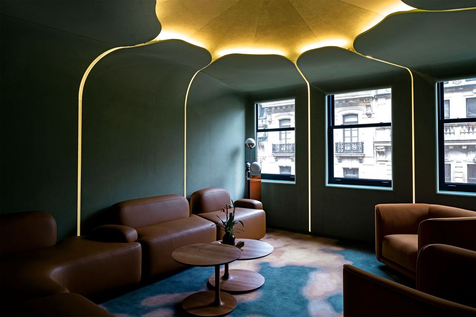 room lounge with dark blue walls and complimentary brown leather sofas and a jellyfish like golden yellow light scheme centered in the ceiling and dripping along the walls
