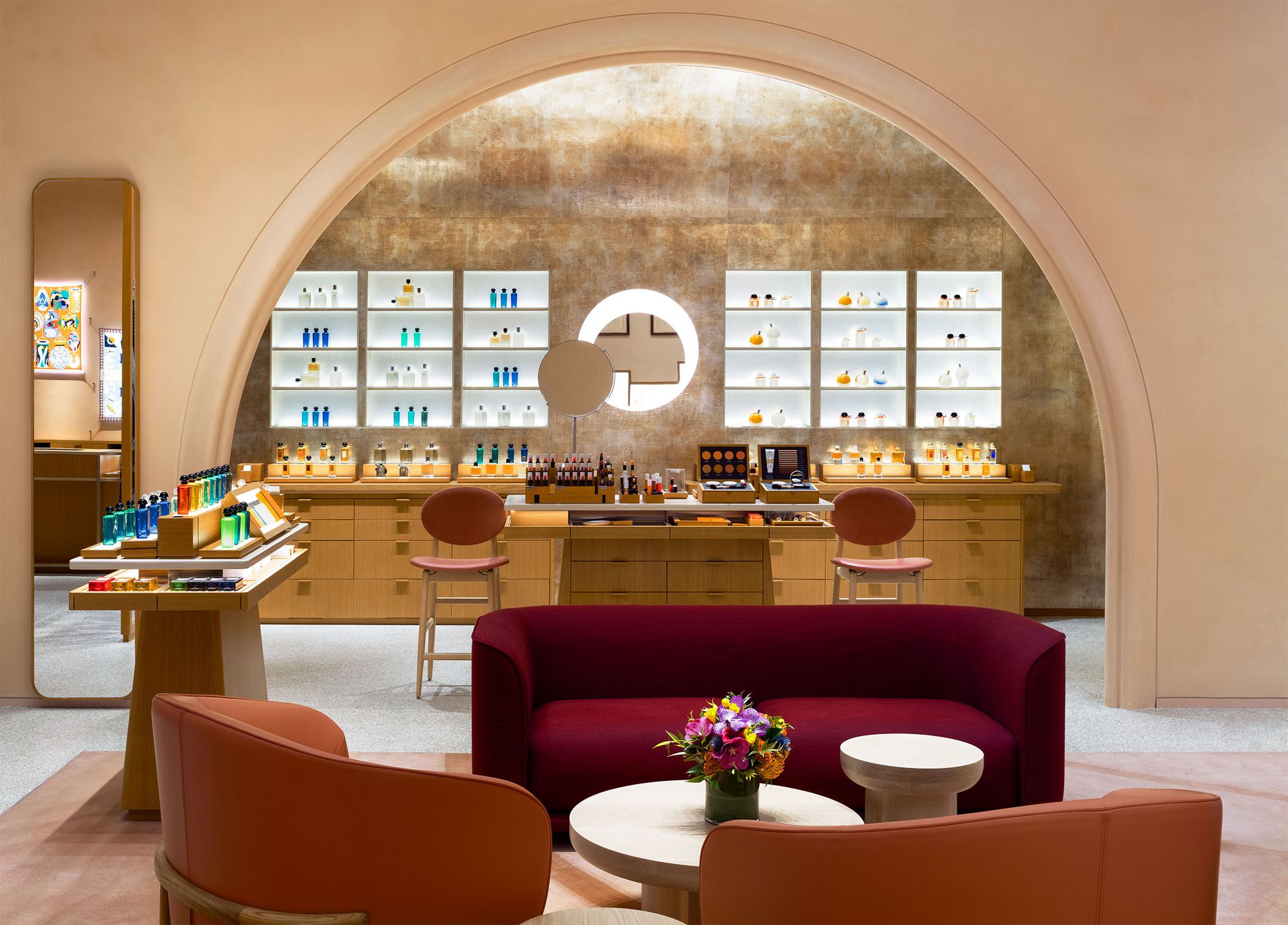 store interior with a large pink arch with glass cases and wooden drawers behind it and in the foreground is an intimate seating area with red and orangy pink velvet upholstered rounded sofa and rounded low armchairs