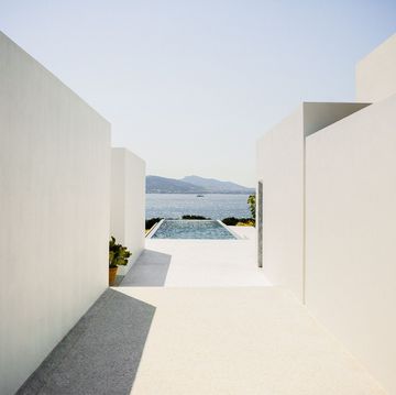 concrete walls on either side lead to the rectangular pool which juts out and overlooks bushes and the sea and mountains beyond