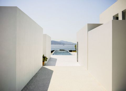 concrete walls on either side lead to the rectangular pool which juts out and overlooks bushes and the sea and mountains beyond