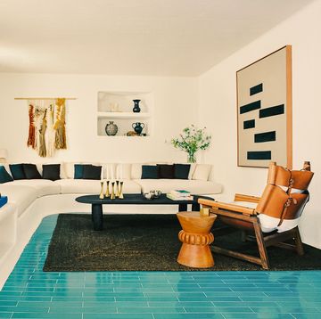 built in white wraparound couch, oval black cocktail table, turquoise tile floor, black rug, drum table and chair in wood and leather with cushions, black shutters, artworks on walls