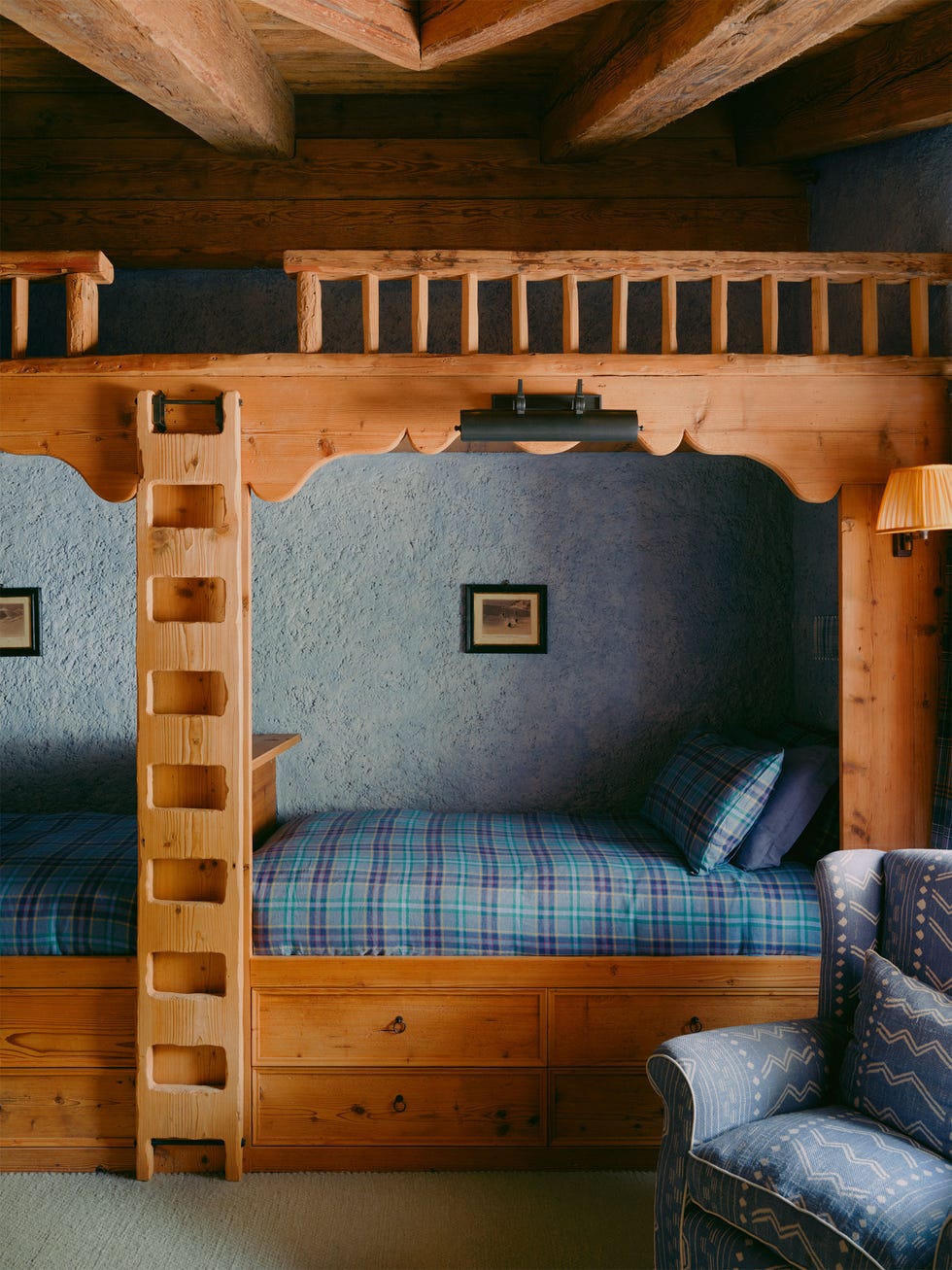 two built in foot to foot beds framed in wood with built in ladder to loft play area on top, storage drawers beneath mattresses in blue and green plaid bedcovers, pillows, blue patterned chair, sconces, light blue textured walls