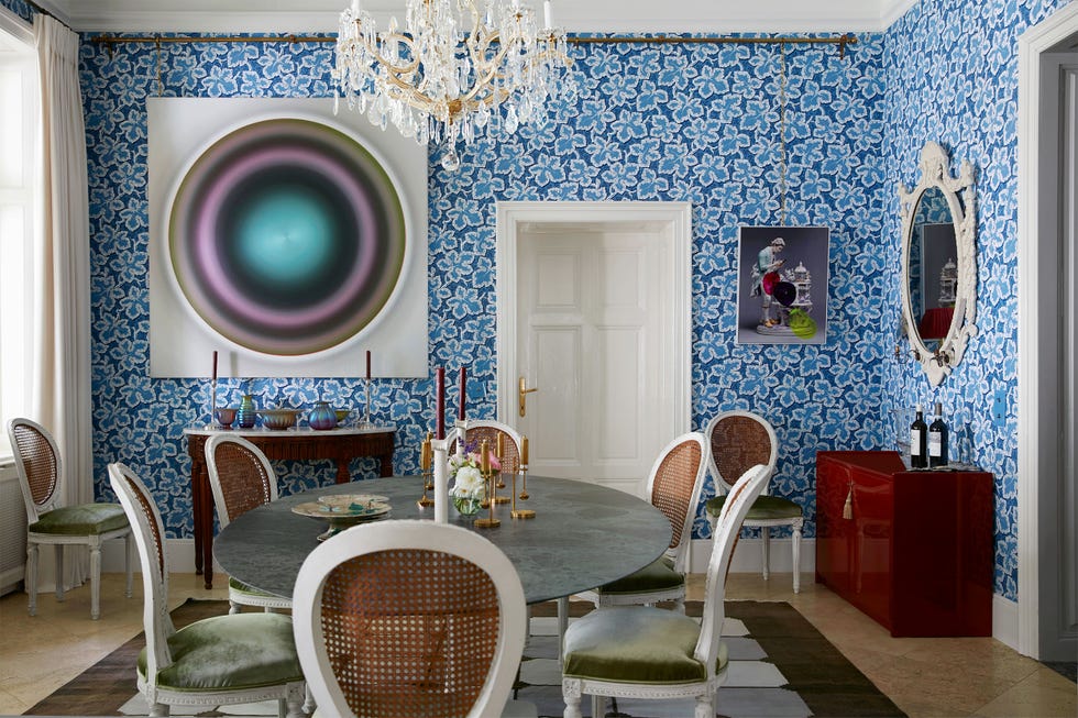 dining table with wicker back chairs in a patterned wallpaper and a large circular colored artwork on the wall