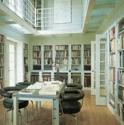 white library with open and glassed shelving and a long metal table with leather chairs pulled up to it and a second floor balcony with more shelving