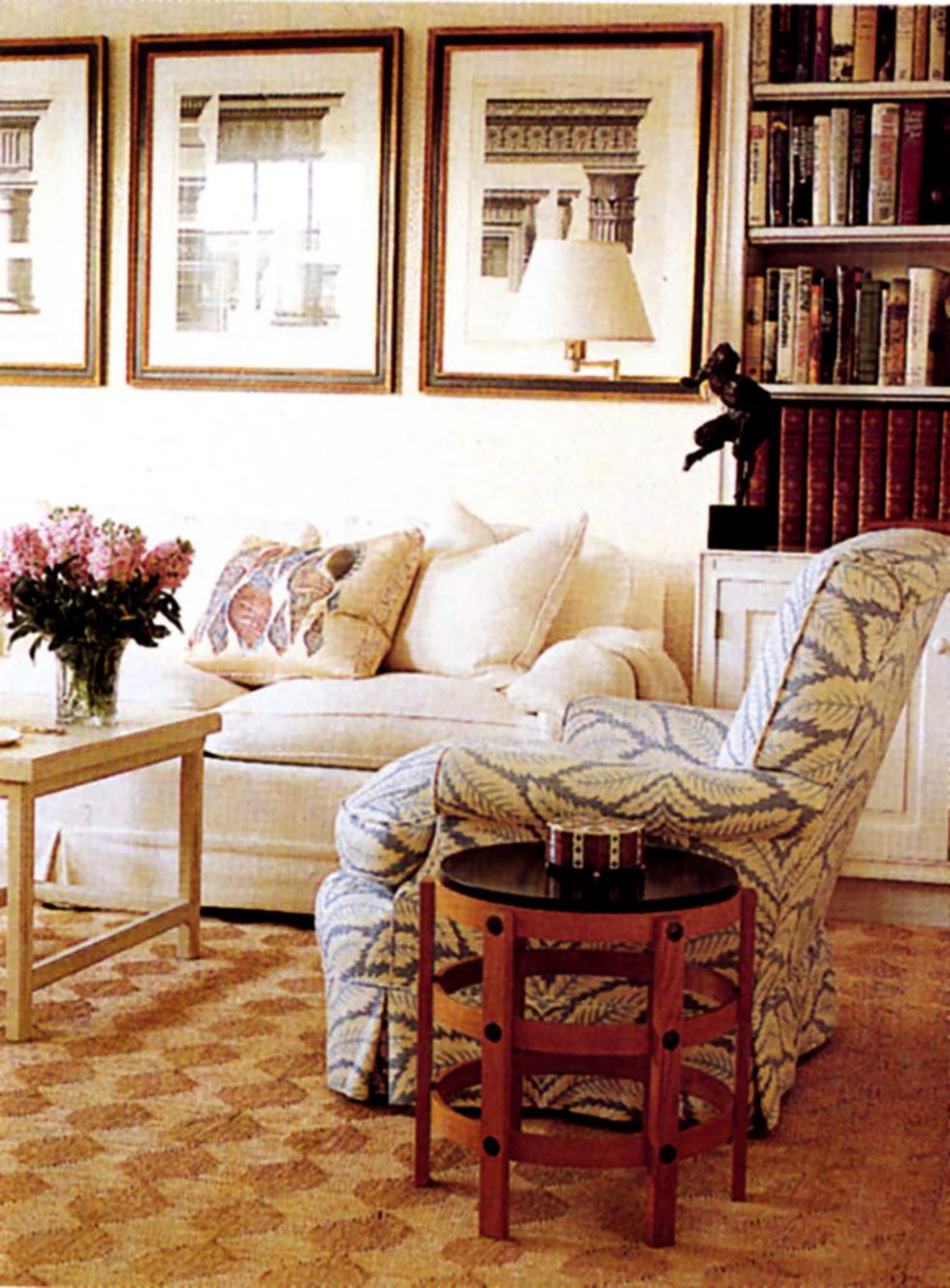 a living room with a sofa and a green patterned armchair and a small table, a side table made of wooden slats and frames on the wall