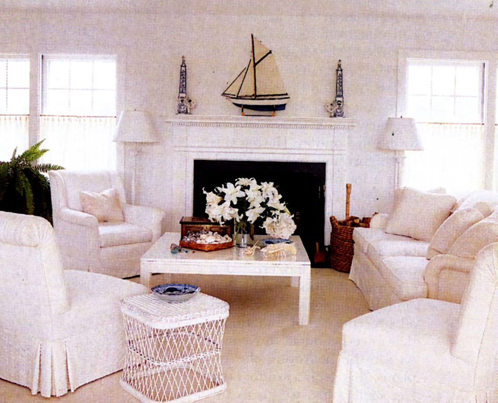 a white living room with fireplace and sofas and chairs, all in white with a white cocktail table in the middle and nautical objects in white