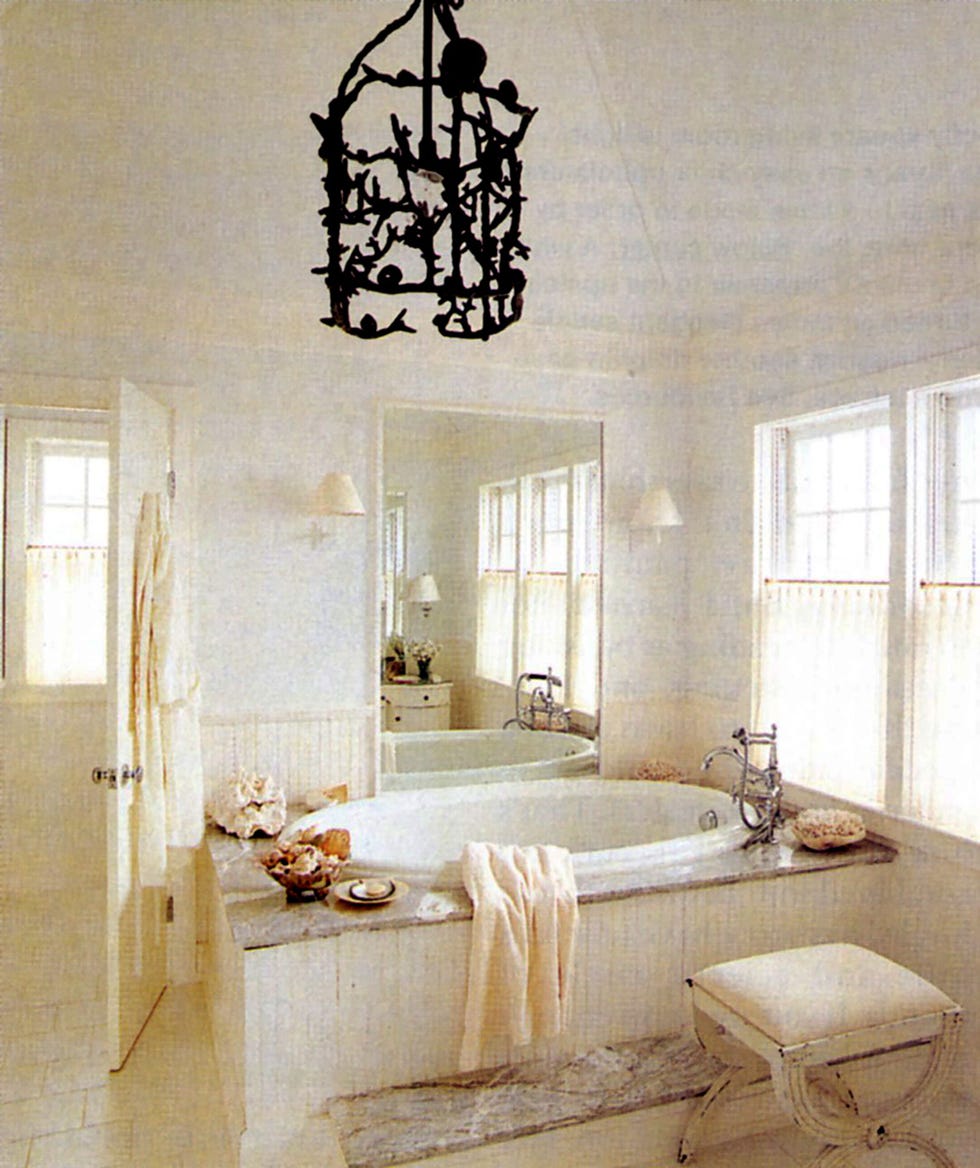 white bathroom with sunken bathtub and X-leg stool and a bronze birdcage chandelier