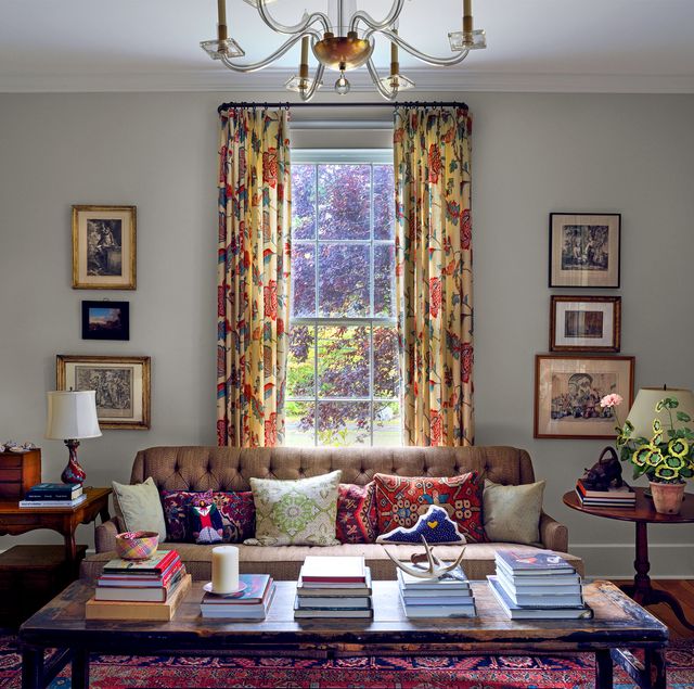 living room with tall windows and curtains, sofa, and table piled with books