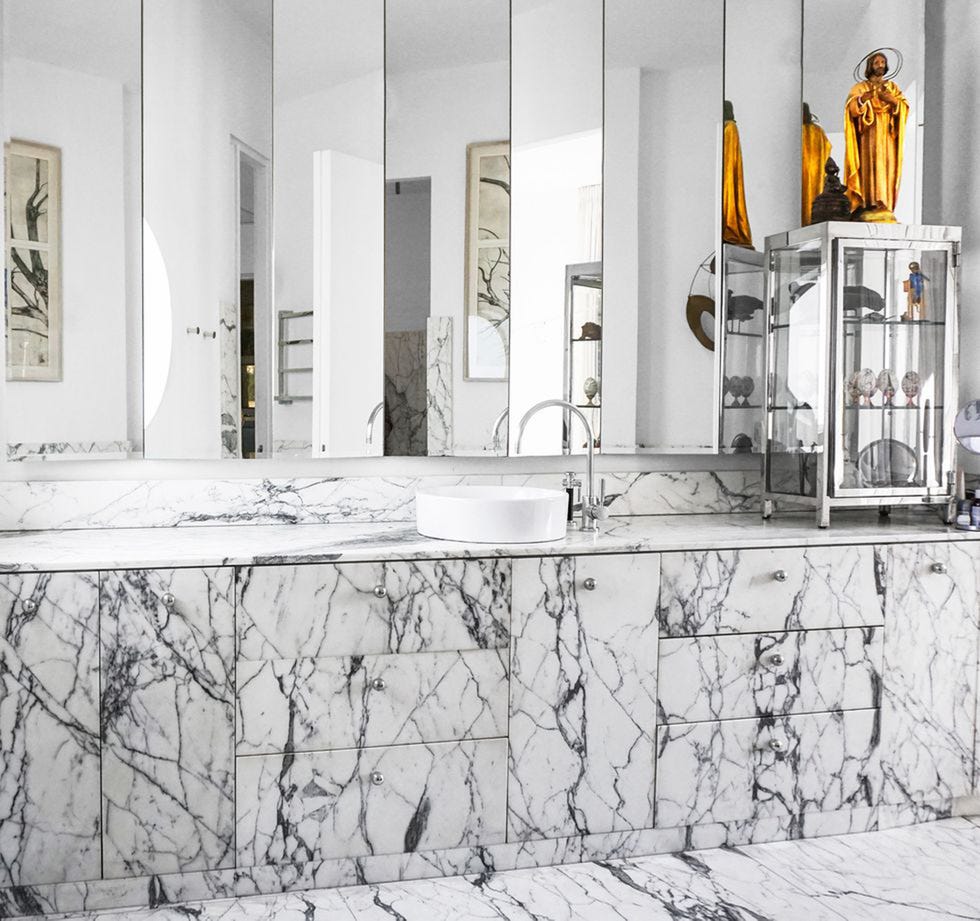 bathroom of house in tel aviv with marble countertops and floors, a glass cabinet, and a religious sculpture