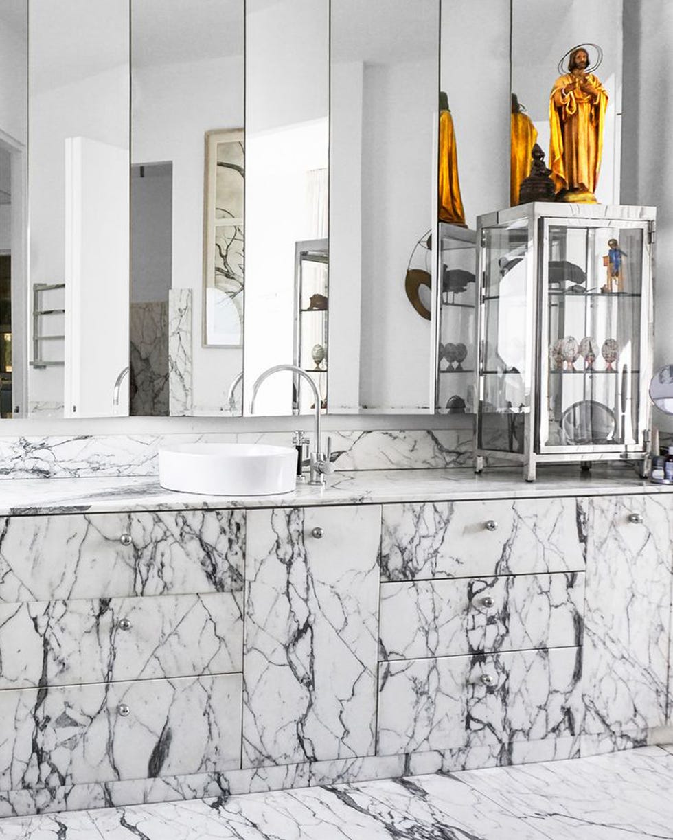 Alex Meitlis & Ivo Bisignano - ELLE Decor bathroom of house in tel aviv with marble countertops and floors, a glass cabinet, and a religious sculpture