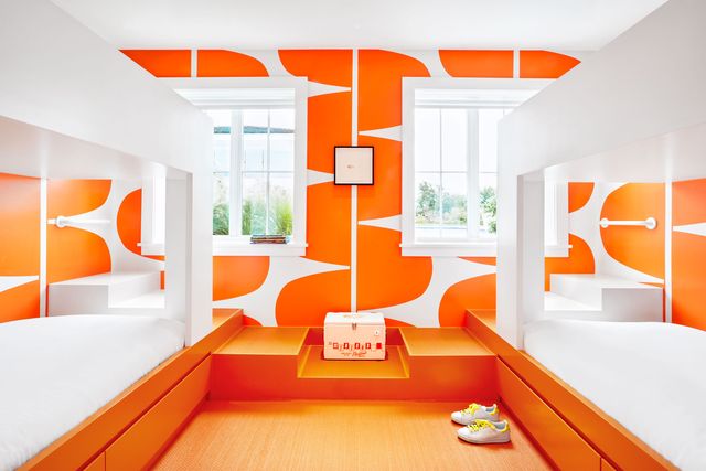 bedroom with white bunk beds and bright orange bases with orange patterned wallpaper at the back surrounding two windows