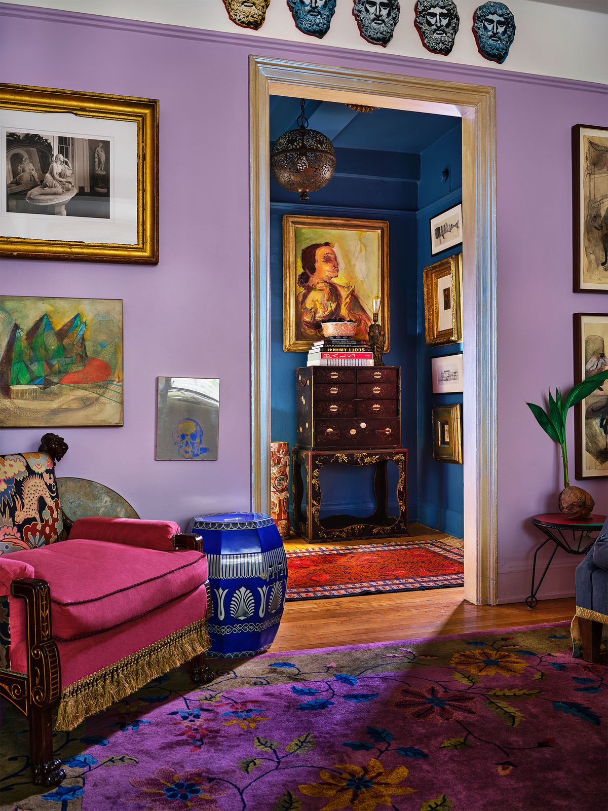 living area with a purple print rug, lilac colored walls, a magenta victorian chair, and blue antique side table, also a view into the entry all with deep blue walls, antique japanese cabinet, and paintings on walls