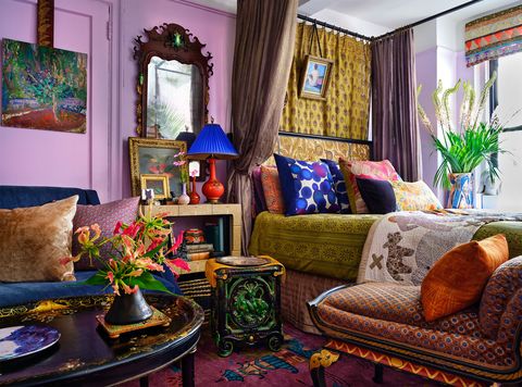 living area with blue velvet sofa and silk pillows, a papier mache cocktail table and antique majolica side table, four poster bed with curtains and pillows covered in dries van noten dresses