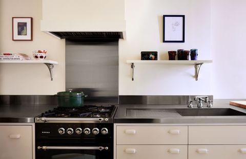 stainless stove set into stainless steel counters with light colored cabinets with small shelving above with small framed artworks