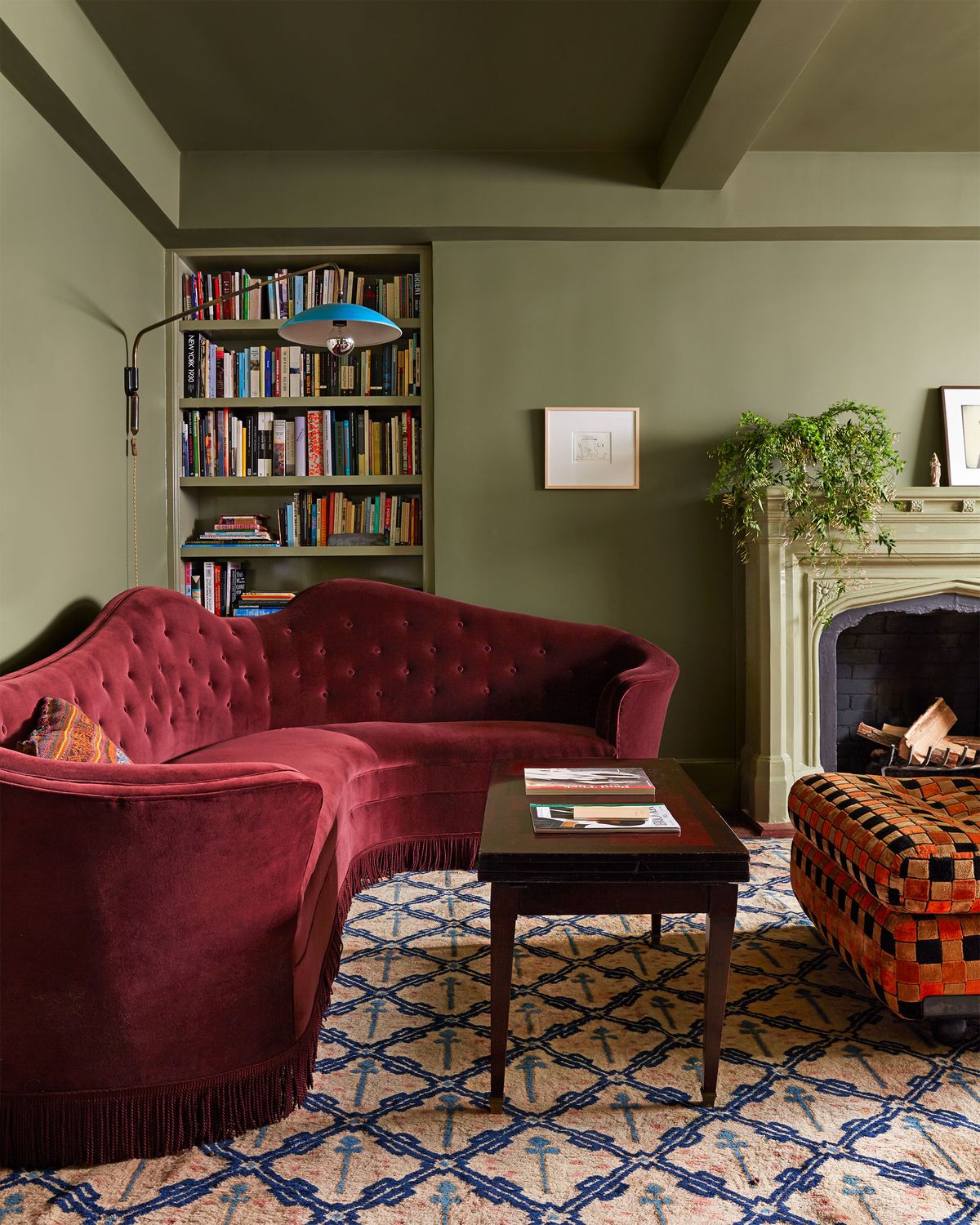 living area with dark green walls and a wraparound sofa in dark reddish orange, a center coffee table and large ottom in orange and brown check fabric on a patterned area rug