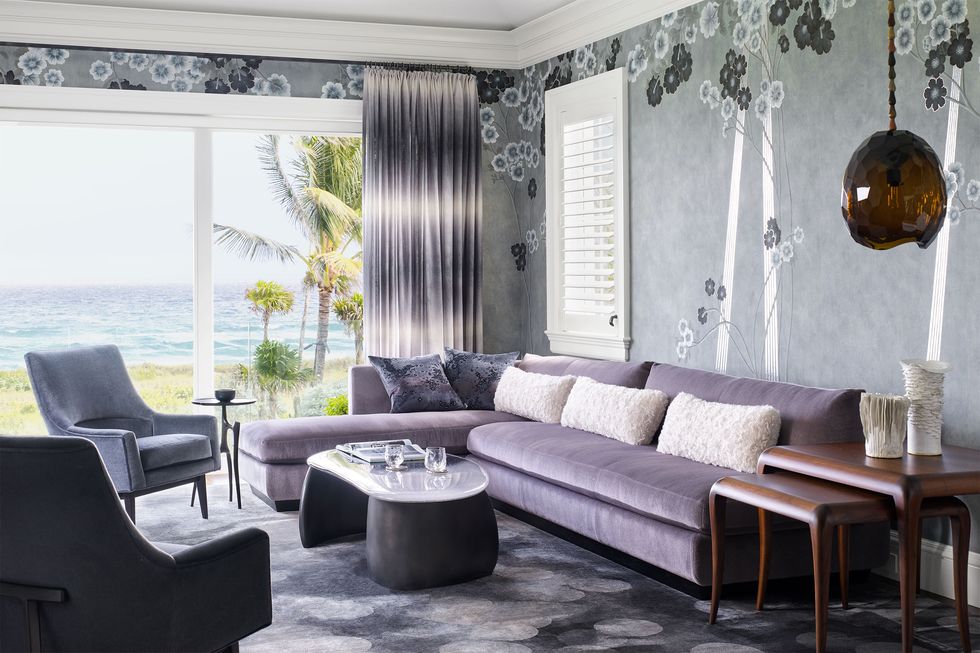 bedroom sitting room with windows facing the shore, gray wallpaper with modern flower pattern, a lilac sofa, cocktail table and two armchairs