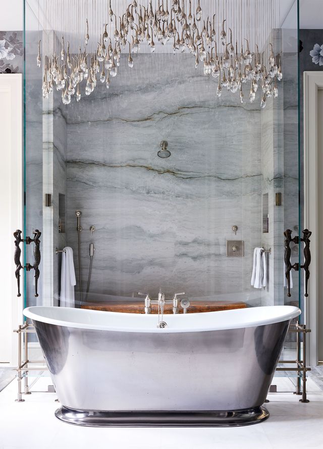 in the primary bathroom is a tub with a silver finish and a chandelier above it, the shower has glass doors with mermaid handles