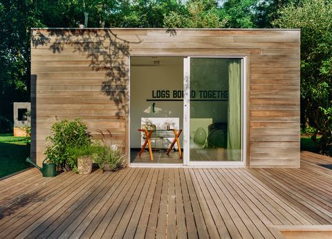 rectangular wood poolhouse with glass doors leading out to a wood deck, a wall sculpture inside reads logs bound together