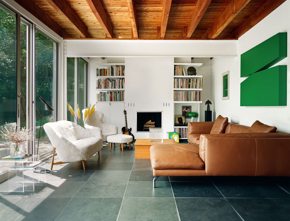 living room with sliding glass doors and love seat and matching chair at left, fireplace with bookshelves above left and right, leather couch at right with green artwork on wall above it