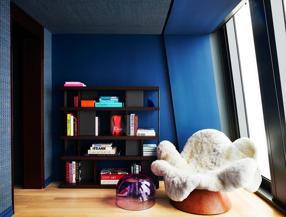 in a bedroom with deep blue walls is a chair covered in a faux white animal skin with arms and legs and a cherry wood base, and black shelves