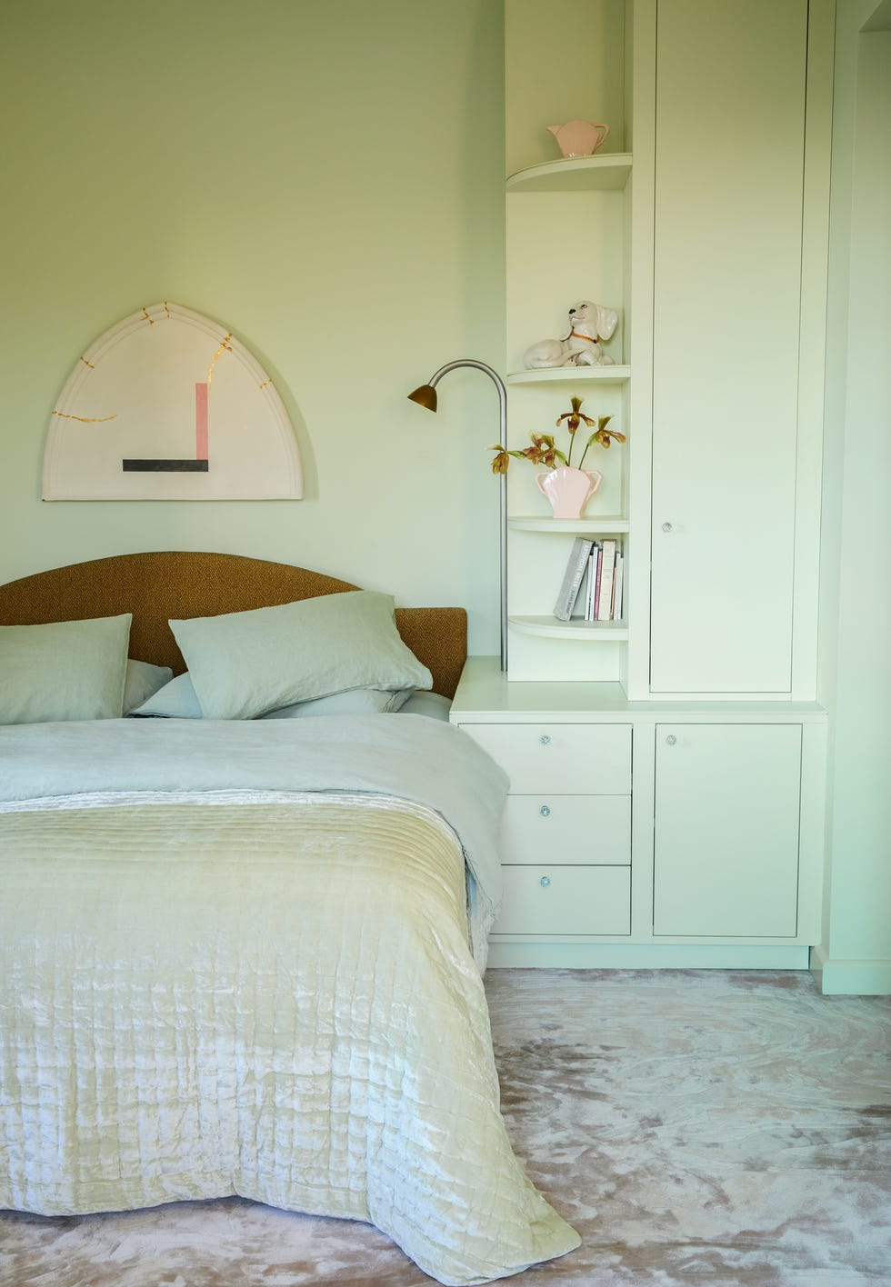 bedroom with green walls and velvet carpet triangular bookcases in one corner of the room and the bed is upholstered in a mustard colored fabric the bed quilt is mint green
