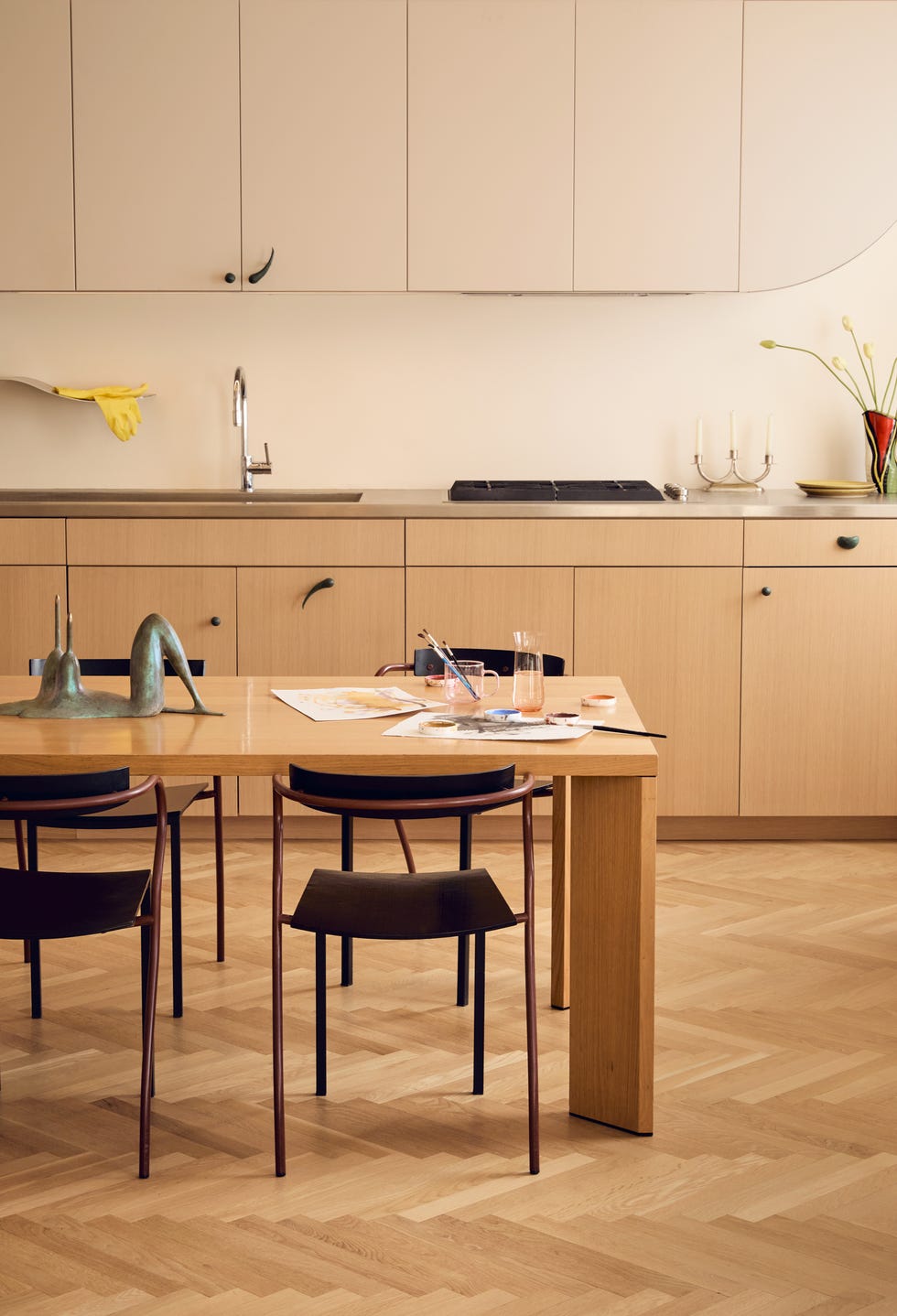 kitchen featuring wood paneled cabinets with iron hardware made to resemble punctuation marks the dining table is also wooden with a set of watercolors on top