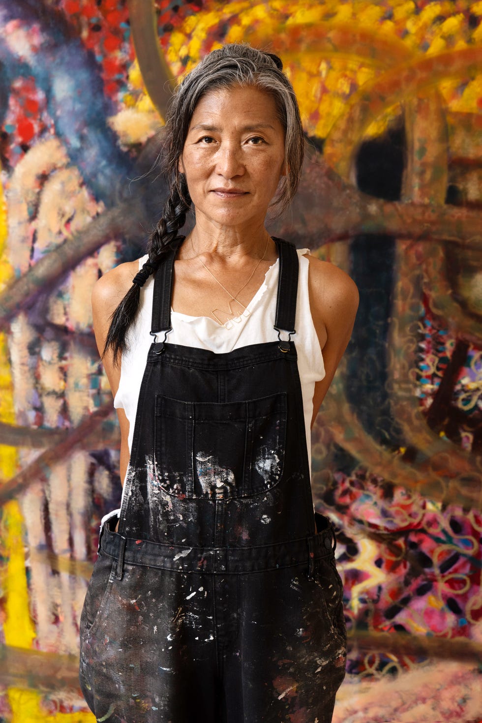 artist wearing paintsplattered overalls against a colorful background