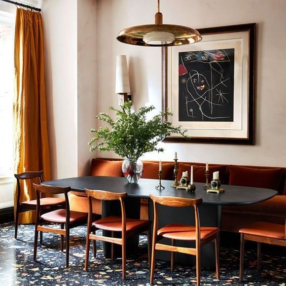 dining area with long dark orange leather banquette and matching chairs pulled up to a dark wood table with rounded corners