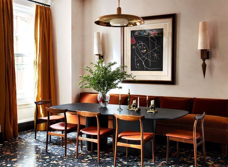 dining area with long dark orange leather banquette and matching chairs pulled up to a dark wood table with rounded corners