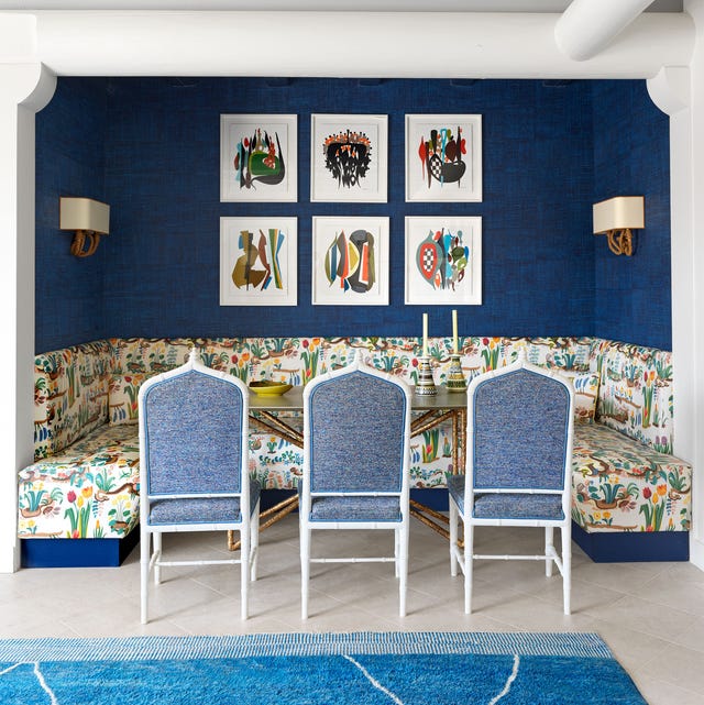 dining table set into an alcove where fabric cushioned chairs face a three sided banquette covered in a spring print fabric, two sconces and colorful framed artwork hang on deep blue walls behind the banquette