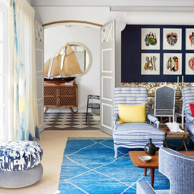 living area with blue criss cross rug and stripped armchairs and a blue swashed pouf looking into another room with checkerboard floor and rattan sideboard agains the wall