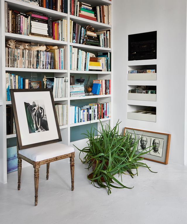 library with book shelves, built in screen and storage drawers, framed photographs on a chair and the floor