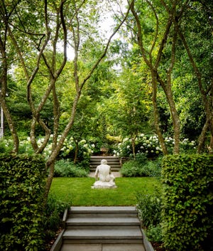 lush garden with low stairway leading to a small patch of lawn with a statue at center and trees and flowering bushes and other hedges flanking it and beyond