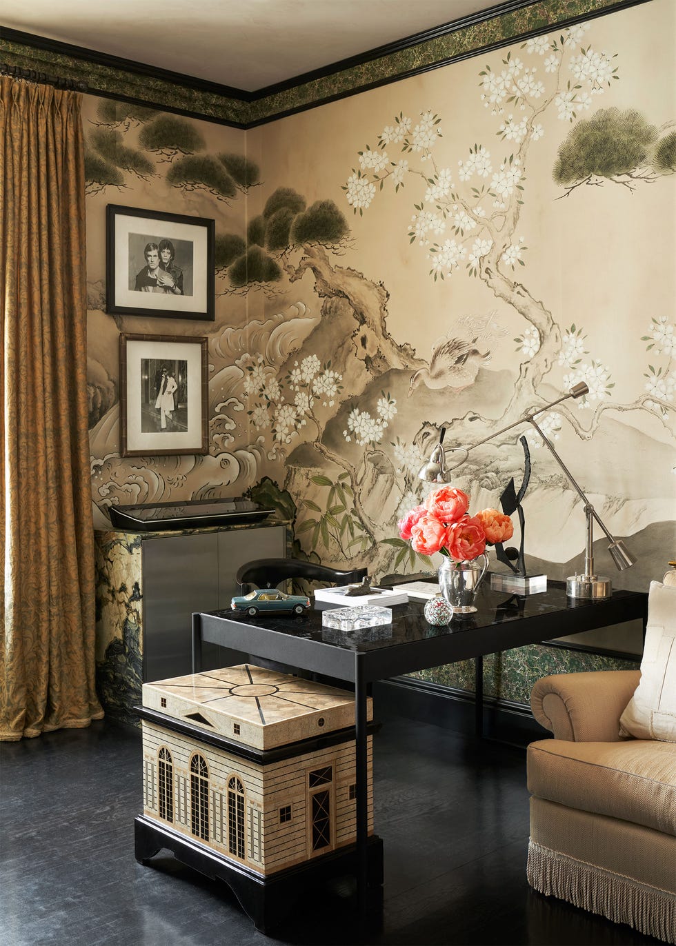 in a corner is a dark marble and metal desk with vase of orange peonies, a desk lamp and other objects, a mini model house sits next to table, two framed photos, japanese screen wallcovering,