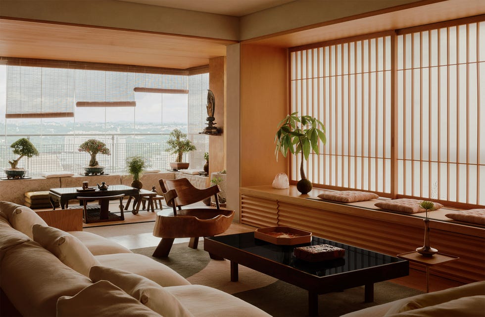 japanese style living room with built in wood storage and window seat with cushions, vertical slats on windows, sofa, cocktail table, chair made from a tree trunk, windows with bamboo blinds, bonsai trees