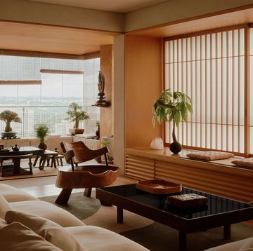 japanese style living room with built in wood storage and window seat with cushions, vertical slats on windows, sofa, cocktail table, chair made from a tree trunk, windows with bamboo blinds, bonsai trees