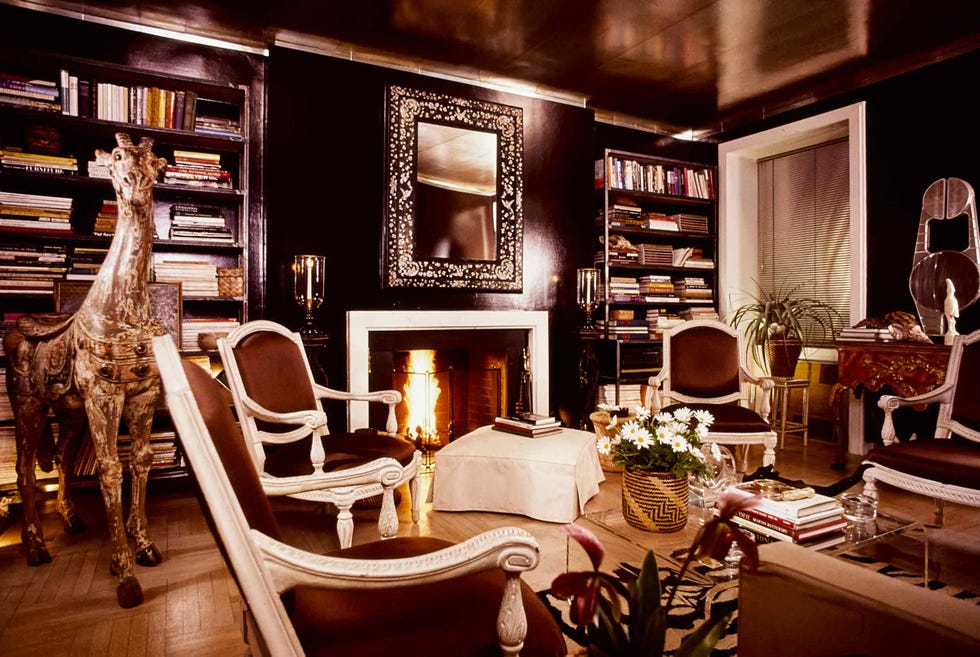 living room with a chinese tea papered ceiling and dark brown walls with mirrored cornices and bases, in the new york city apartment of interior designer albert hadley. a 17th century mirror hanging over the fireplace, a wooden giraffe and a japanese aluminum sculpture displayed on a portuguese console table with human like legs in high topped shoes, round out the decor. *** local caption ***
