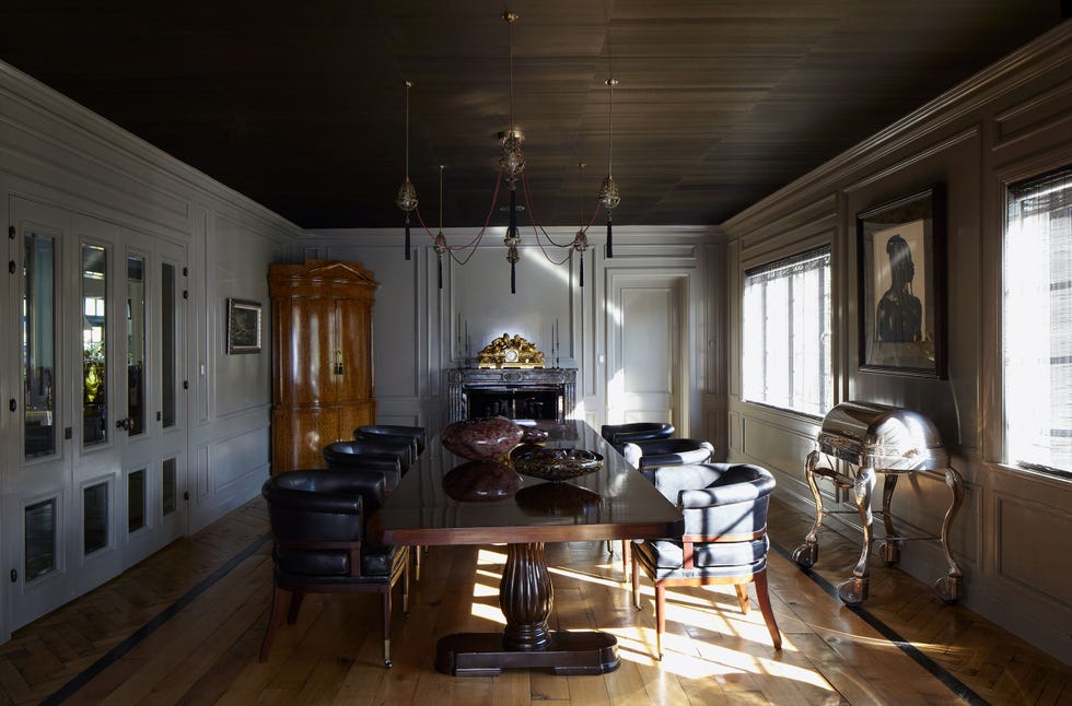 a long dining room a simple chandelier and double pedestal table and inset molding on the walls and round back upholstered chairs at the table