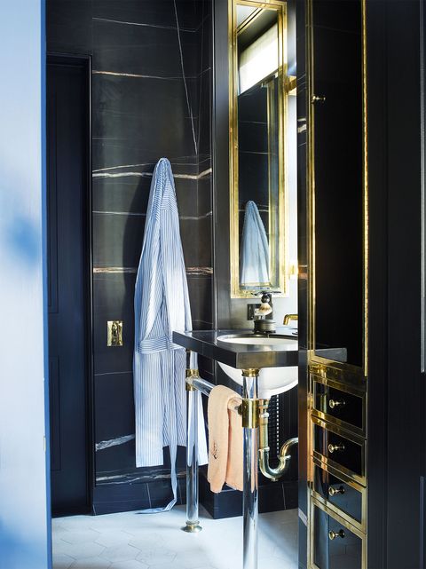 masculine bathroom with dark blue cabinets and silver and gold tone sink and a pinstripe robe hanging from door