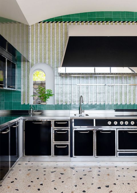 a kitchen with green backsplash and chrome and black appliances and cabinets