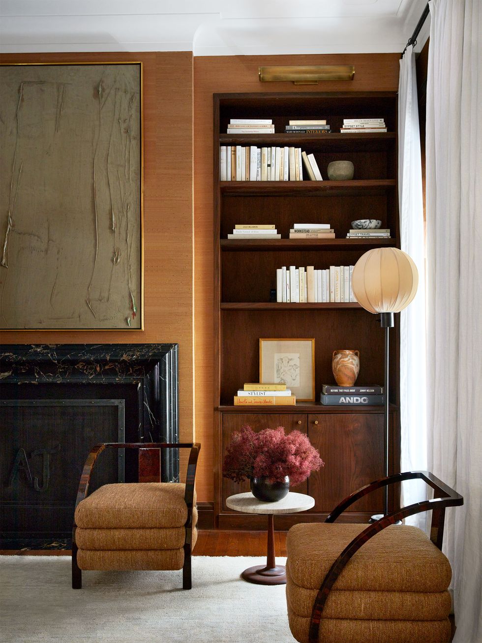 The corner of the bedroom has two chairs with three seat cushions each, a small round marble top pedestal table, a floor lamp with a globe shade, a built-in bookshelf, and a black marble fireplace.