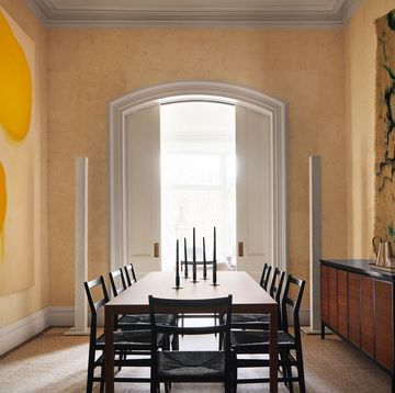 a dining room with ocher colored textured walls, large abstract artworks on facing walls, wood dining table with eight chairs, candelabra, sideboard of dark wood, arched doorway with sliding doors to a terrace