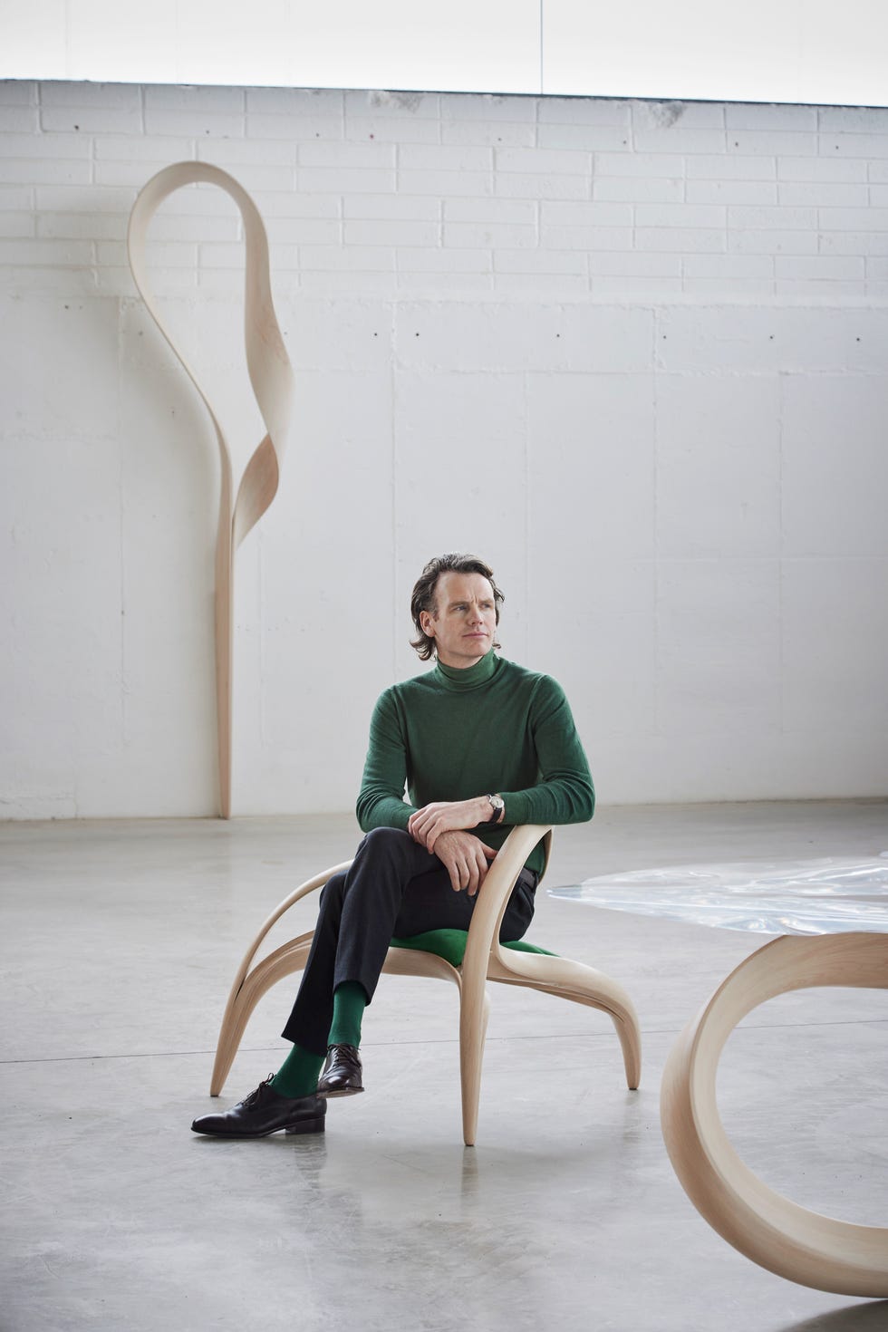 a man seated in a minimalist wooden chair against a simple background
